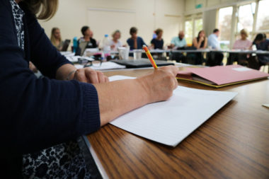 A picture of people around a table. In the foreground a person is taking notes. Research Design Service East of England