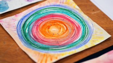 An image of artwork - a circle made up of rainbow colours with yellow in the middle, gradually getting larger with blue on the outer edge